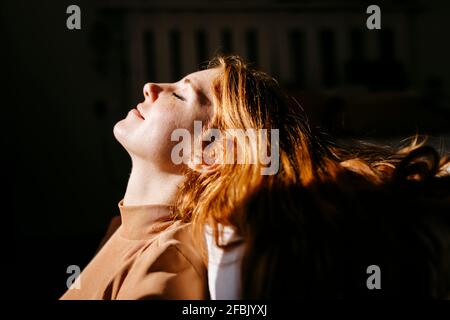 Donna sorridente che si appoggia a casa sotto la luce del sole Foto Stock