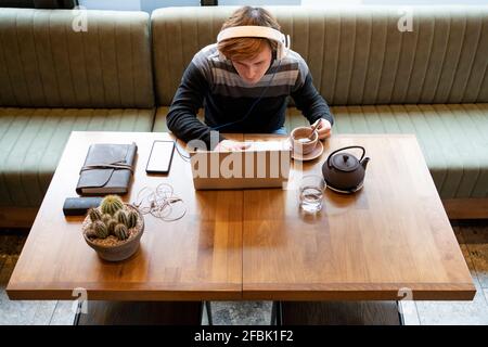 Uomo d'affari che usa un computer portatile da teacup mentre si siede alla scrivania ufficio Foto Stock