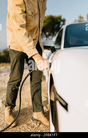 Uomo che carica l'auto elettrica durante il viaggio su strada Foto Stock