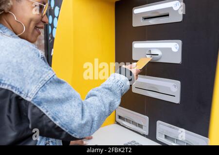 Donna sorridente che inserisce la carta di credito nella macchina ATM Foto Stock