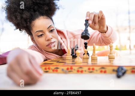 Donna concentrata che gioca a scacchi mentre si appoggia al tavolo Foto Stock