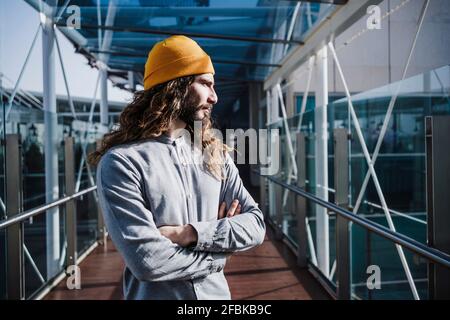 Uomo premuroso con le braccia incrociate guardando via alla luce del sole a. luogo di lavoro Foto Stock