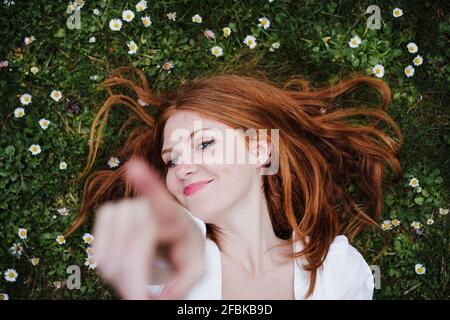 Sorridente giovane donna che punta mentre si sdraiava sull'erba Foto Stock