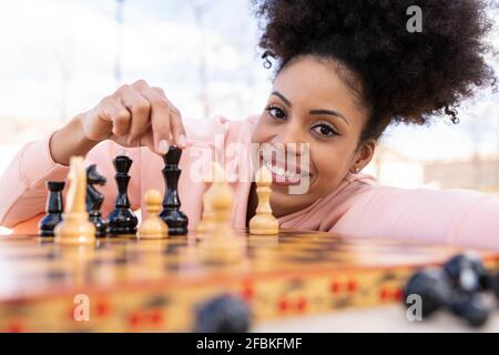 Donna sorridente che gioca a scacchi mentre si appoggia al tavolo Foto Stock