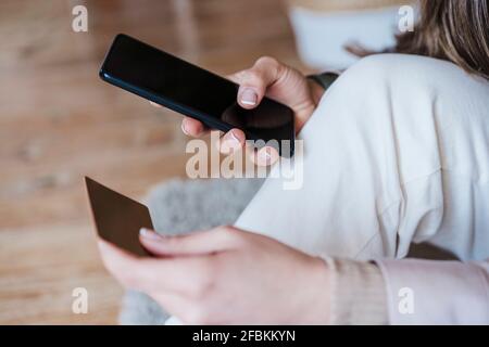 Mani di donna che usano lo smartphone mentre pagano dal credito carta a casa Foto Stock