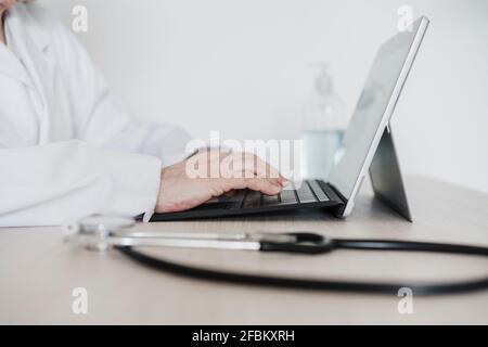 Dottoressa senior che lavora su tablet digitale alla scrivania ospedale Foto Stock