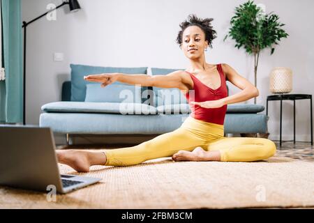 Donna che fa yoga mentre si guarda tutorial online su computer portatile a. casa Foto Stock