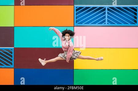 Ballerina femminile che salta con le gambe divaricate davanti a multi parete colorata Foto Stock