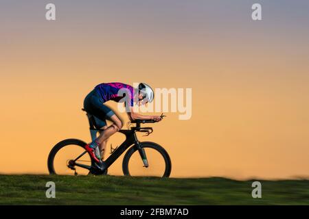Triathlon sportivo maschile in bicicletta a terra durante il tramonto Foto Stock