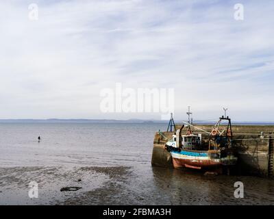 Il peschereccio da traino di gamberi si è legato all'ingresso del porto con la bassa marea a Fisherrow, vicino a Edimburgo, con una persona che ha un piggy di ritorno in acqua. Foto Stock