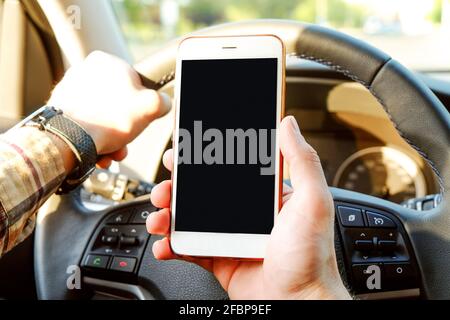 Giovane uomo che tiene il telefono delle cellule dello schermo vuoto mentre guida l'automobile. Mano maschile del conducente sul volante e controllo del suo smartphone in un veicolo in movimento. Non Foto Stock