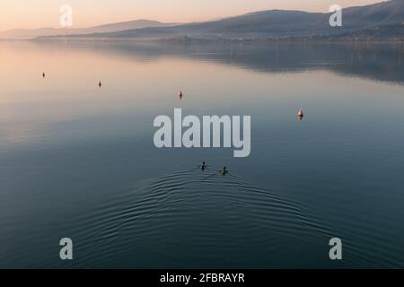 Vista tranquilla e da sogno di un lago, con anatre, boe e colline riflessi sull'acqua Foto Stock