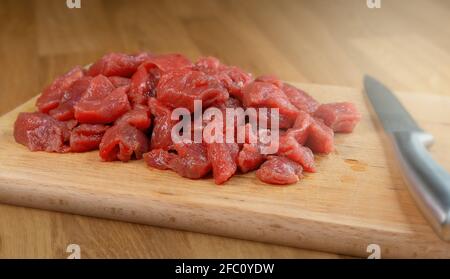 Carne cruda di vitello tagliata a piccoli pezzi su un legno tagliere con un coltello accanto ad esso Foto Stock