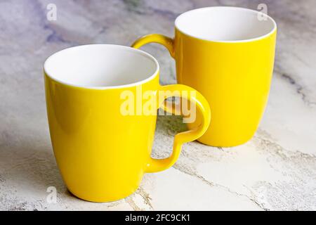Due tazze da tè vuote di colore giallo brillante su sfondo di un tavolo da cucina in marmo. Foto Stock