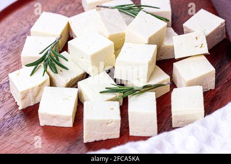 Cubetti di tofu vegetariani biologici crudi con rosmarino fresco su sfondo di legno. Foto Stock