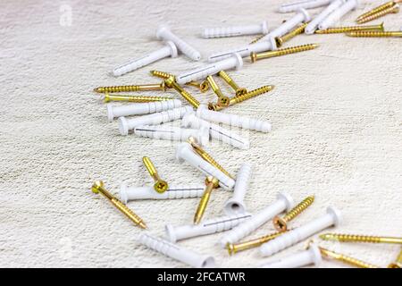 Molti tasselli in acciaio e plastica per la riparazione su fondo in cemento grigio chiaro con spazio di copia. Fai da te, miglioramento della casa e concetto di costruzione della casa. Foto Stock