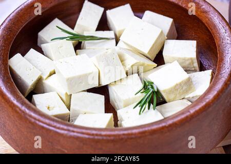 Cubetti di tofu vegetariani biologici crudi in ciotola rotonda di legno con rosmarino fresco. Foto Stock