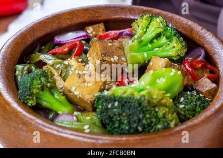 Tofu fritto vegetariano fatto in casa con verdure (broccoli, pepe, cipolle e fagioli verdi) nella ciotola di legno. Foto Stock