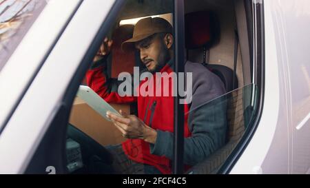 Buon corriere indiano utilizzando la tavoletta nel furgone . Foto di alta qualità Foto Stock