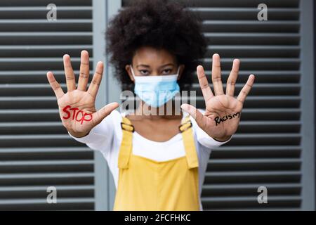 Ritratto di donna di razza mista che indossa maschera faccia facendo sosta gesto con mani coperte per iscritto Foto Stock