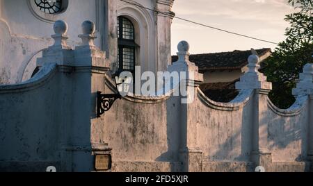 L'edificio della vecchia chiesa coloniale e le pareti bianche esterne con una lampada da strada a fuoco mentre la luce della sera illumina il muro. Foto Stock