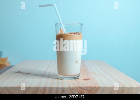 Bicchiere da caffè Dalgona fatto in casa su un tavolo in legno testurizzato. Caffè istantaneo con latte fresco, per preparare la deliziosa bevanda coreana. Alla moda Foto Stock