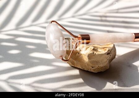 Rullo facciale in quarzo rosa cristallo su pietre, sfondo in marmo. Massaggio viso anti-age per un trattamento naturale di sollevamento e tonificazione a casa. Conce di bellezza Foto Stock