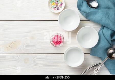 Ciotole bianche vuote, un cucchiaio di gelato e dolci dolciari su sfondo bianco di legno. Vista dall'alto, orizzontale. Un concetto per il tuo progetto. Foto Stock