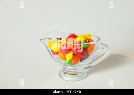 Caramelle colorate in un piccolo vaso di vetro su un bianco sfondo Foto Stock