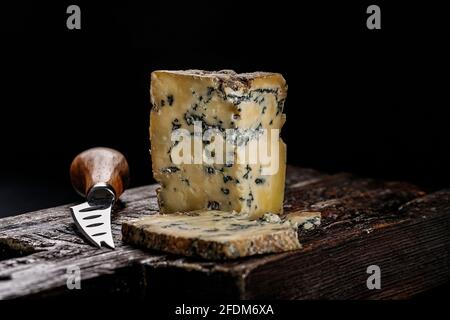 Formaggio semi-morbido con muffa di latte di mucca. Il re dei formaggi blu è Stilton. Pezzo di formaggio su una tavola di legno scuro e coltello per tagliare la chee Foto Stock