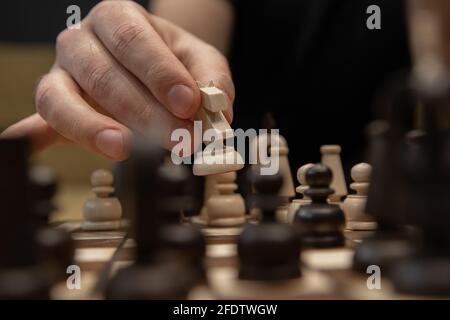 Mano che prende il passo successivo sul gioco di scacchi. Pezzo di cavaliere bianco di legno che si muove con la mano umana Foto Stock