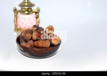 Datteri secchi frutta in una ciotola di legno isolata su uno sfondo bianco con una lanterna islamica di Ramadan (Fanoos Ramadan), datteri secchi utilizzati nella colazione i Foto Stock