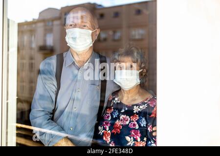 Coppia anziana preoccupata che guarda attraverso la finestra a casa durante il coronavirus COVID-19 epidemia Foto Stock