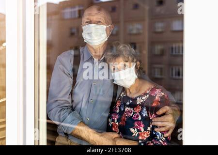 Coppia anziana preoccupata che guarda attraverso la finestra a casa durante il coronavirus COVID-19 epidemia Foto Stock