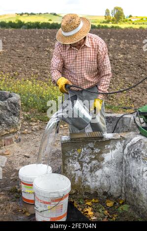 Coltivatore con cappello di paglia che attingeva acqua fresca da un pozzo nel contryside. Foto Stock