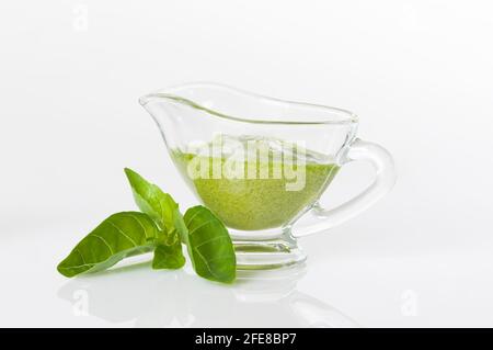 Delizioso pesto fresco preparato con basilico, olio d'oliva, aglio e pinoli. Salsa di pesto verde in una barca con sugo su sfondo bianco. Foto Stock