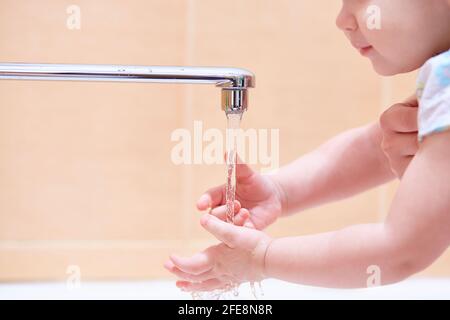 Primo piano di un bambino che si lava le mani sotto l'acqua corrente da un rubinetto metallico. Foto Stock