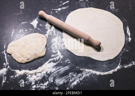 pasta per pizza che viene arrotolato su banco da cucina con forno in background, concetto di ingredienti semplici naturali sani Foto Stock