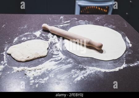 pasta per pizza che viene arrotolato su banco da cucina con forno in background, concetto di ingredienti semplici naturali sani Foto Stock