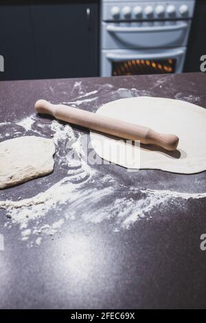 pasta per pizza che viene arrotolato su banco da cucina con forno in background, concetto di ingredienti semplici naturali sani Foto Stock
