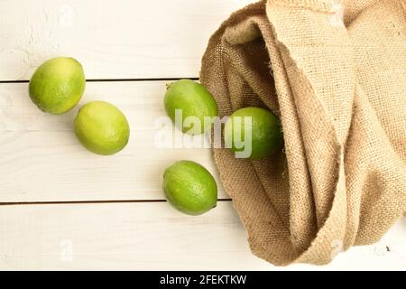 Diverse gustose lime organiche con sacchetto di iuta, su un tavolo di legno dipinto. Foto Stock