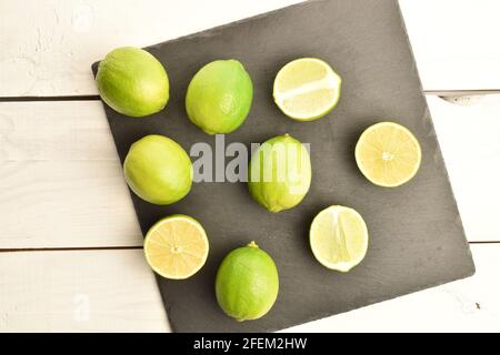 Alcune intere e diverse metà di calce succosa su una tavola di ardesia, su un tavolo di legno dipinto. Foto Stock