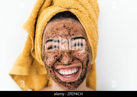 Giovane donna sorridente che applica la maschera di scrub del caffè sul viso - ragazza felice che ha la cura della pelle spa giorno a casa Foto Stock