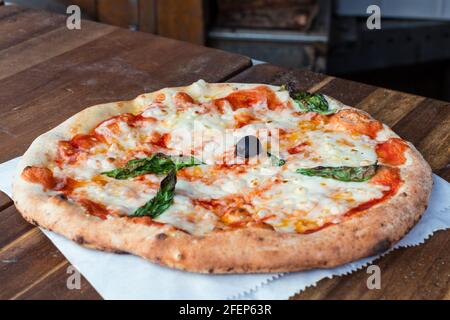 Pizza Margherita appena sfornata su fondo di legno rustico scuro, fuoco selettivo, primo piano Foto Stock