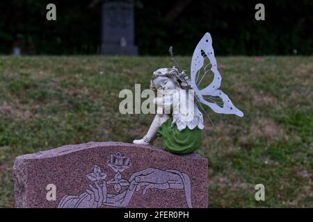 Una figurina di angelo dolce sulla cima di una lapide in un cimitero della chiesa - sfondo verde erba Foto Stock