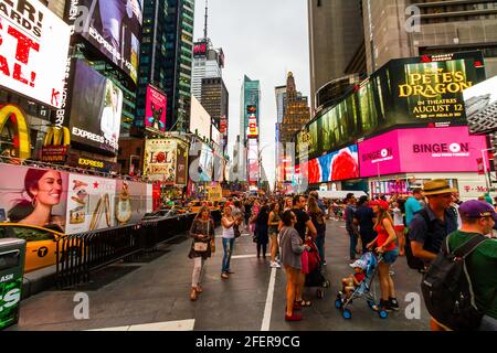 Turisti in abiti estivi scattare foto a Times Square in una serata intensa Foto Stock
