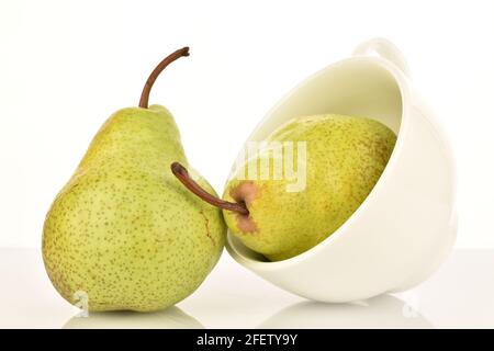 Due pere mature verdi con una tazza bianca in ceramica, primo piano, su sfondo bianco. Foto Stock