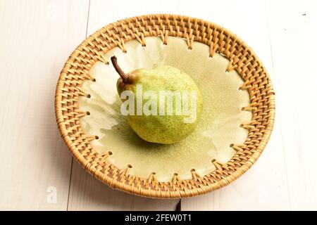 Una gustosa pera verde matura con un piatto in ceramica, primo piano, su un tavolo di legno dipinto. Foto Stock