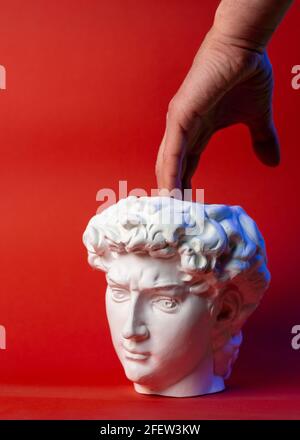 Vaso in gesso sotto forma di testa di Davide e mano maschio su sfondo rosso. Foto Stock