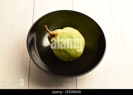 Una gustosa pera verde matura con un piatto in ceramica, primo piano, su un tavolo di legno dipinto. Foto Stock